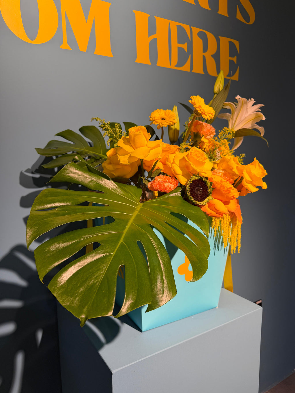Tropical Sunrise signature box arrangement with yellow and orange roses, sunflowers, and tropical monstera leaves