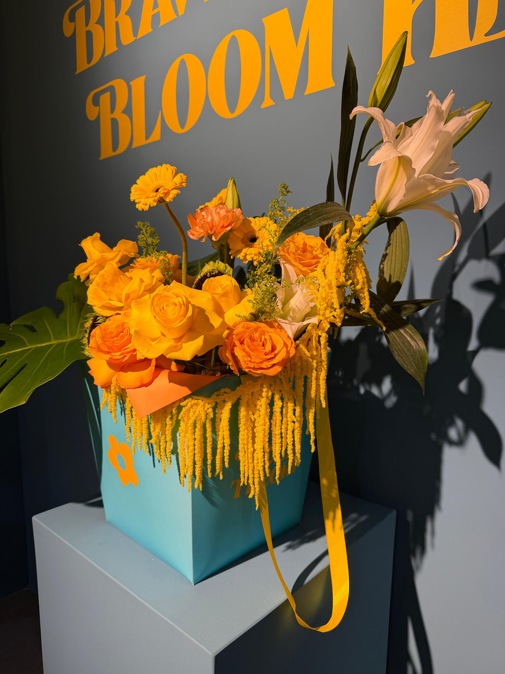 Tropical Sunrise signature box arrangement with yellow and orange roses, sunflowers, and tropical monstera leaves